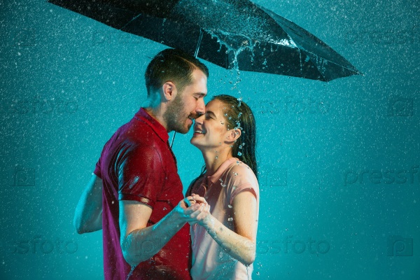 The loving couple in the rain with umbrella on a turquoise background, stock photo
