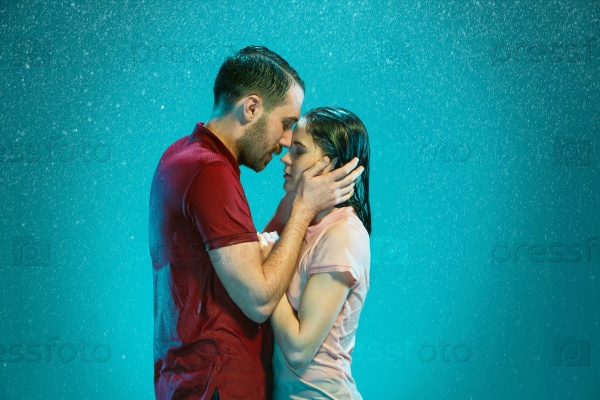 The loving couple kissing in the rain on a turquoise background, stock photo