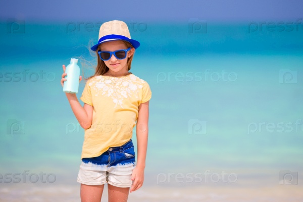 Little adorable girl with suntan lotion bottle on the beach, stock photo