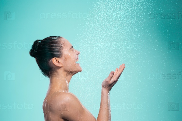 Woman enjoying the water in the shower under a water jet on blue background, stock photo