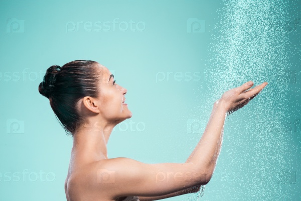 Woman enjoying the water in the shower under a water jet on blue background, stock photo