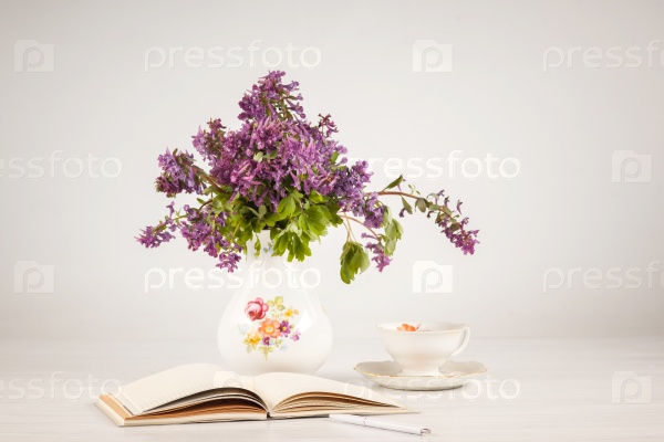 Tea with lemon and bouquet of lilac primroses on the table with open notebook, stock photo