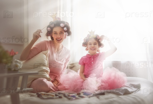 Funny family! Mother and her child daughter girl with a paper accessories. Mother and daughter preparing for a party and having fun. Beautiful young woman and funny girl with a paper crowns on sticks.