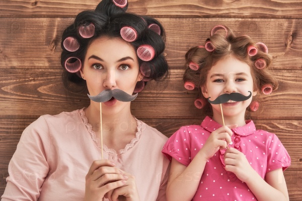 Funny family! Mother and her child daughter girl with a paper accessories. Beauty funny girl holding paper mustache on stick. Beautiful young woman holding paper mustache on stick.