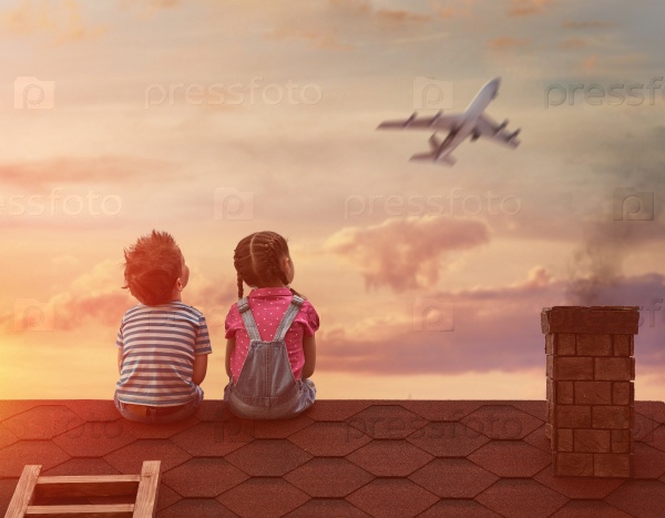 Two little children playing on the roof of the house and looking at the sky and dreaming of becoming a pilots, stock photo