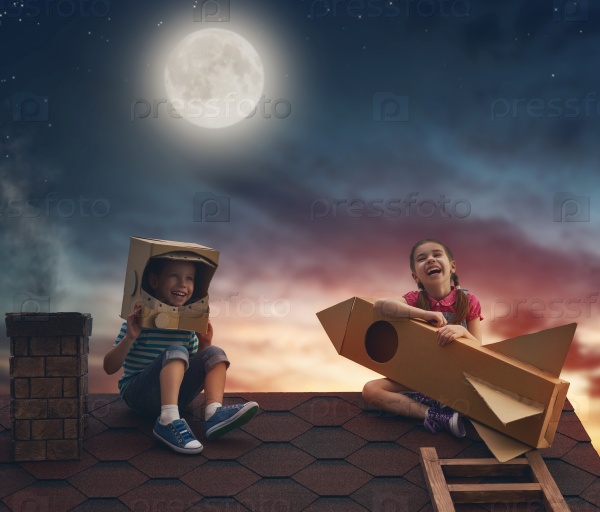 Two little children playing astronauts. Children on the background of moon sky. Child boy in an astronaut costume and child girl with toy rocket standing on the roof of the house and looking at the sky and dreaming of becoming a spacemen, stock photo
