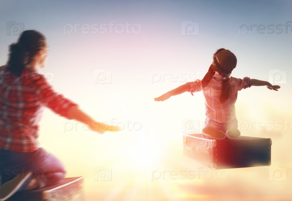 Dreams of travel! Child girl and her mom flying on a suitcase against the backdrop of a sunset, stock photo