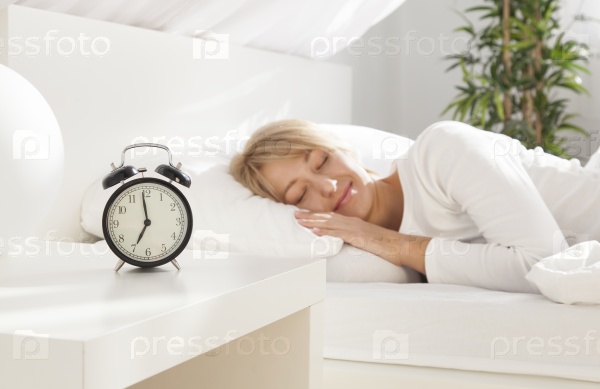 beautiful girl sleeping in her bed. clock on the nightstand. focus on clock