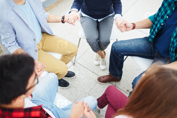 People sitting in circle holding hands in psychology class, stock photo