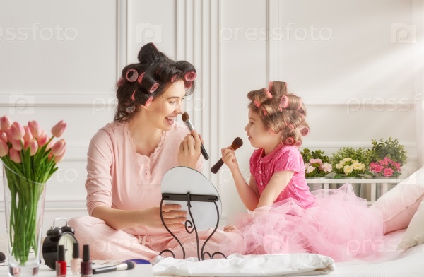 Happy loving family. Mother and daughter are doing hair and having fun. Mother and daughter doing your makeup sitting on the bed in the bedroom.