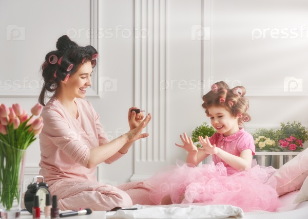 Happy loving family. Mother and daughter are doing hair, manicures and having fun. Mother and daughter sitting on the bed in the bedroom, stock photo