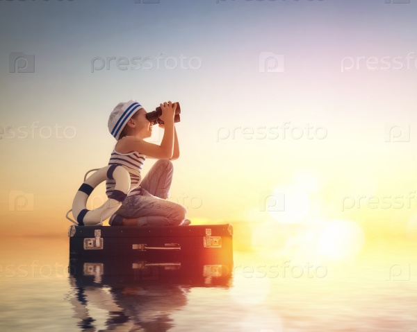 Dreams of travel! Child floats on a suitcase against the backdrop of a sunset.