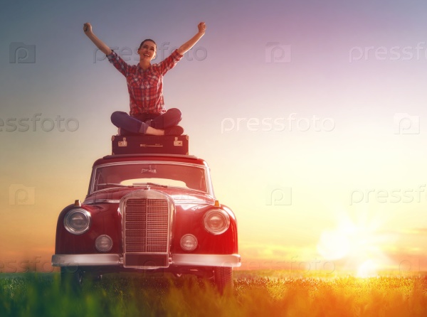 Toward adventure! Girl relaxing and enjoying road trip. Beautiful young woman sitting on roof of vintage car, stock photo