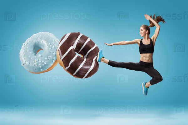 Fit young woman fighting off bad food on a blue background. Concept of diet and healthy lifestile, stock photo