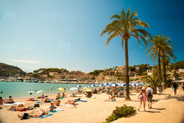 View of the beach of Port de Soller with people lying on sand and the old buildings visible in background, Soller, Balearic islands, Spain.