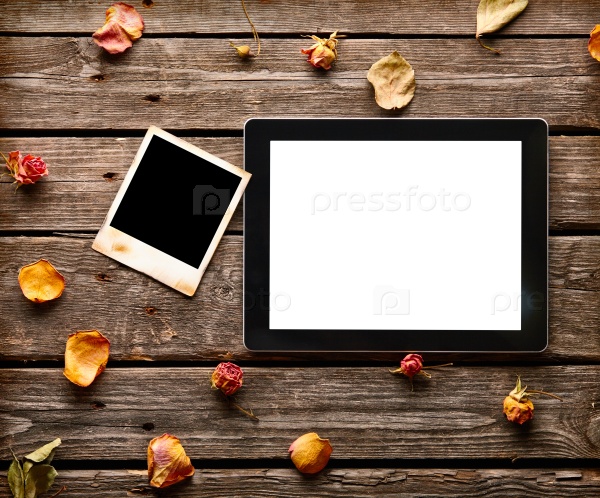 Digital tablet computer with blank instant photo and rose petals on old wooden desk.