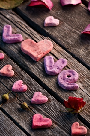 Word Love with rose petals and small heart shaped stuff on old vintage wood plates. Sweet holiday background.