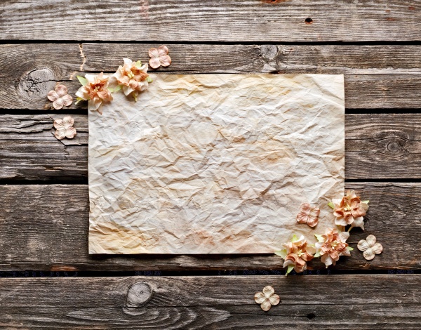 Old crumpled paper with dried flowers or craft flowers on old wood. Sweet holiday background.