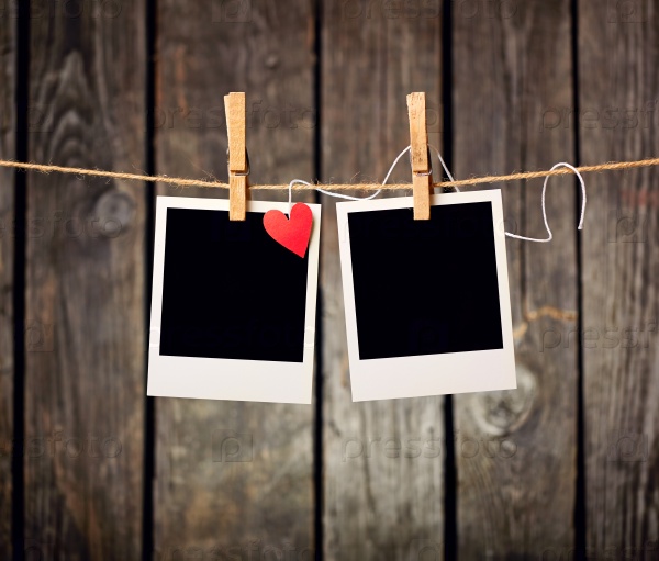 Blank instant photos and small red paper heart hanging on the clothesline. On old wood background.