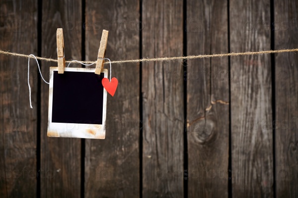 Blank instant photo and small red paper heart hanging on the clothesline. On old wood background.