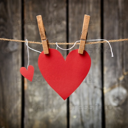 Two lovely red hearts - big and small hanging on the clothesline. On old wood background.