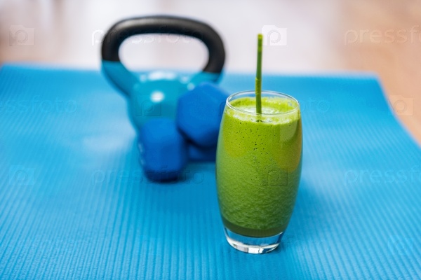 Weight loss healthy eating green vegetable smoothie with free weights kettlebells and exercise mat in gym center. Health and fitness concept. Vegetarian diet and nutrition for strength training.