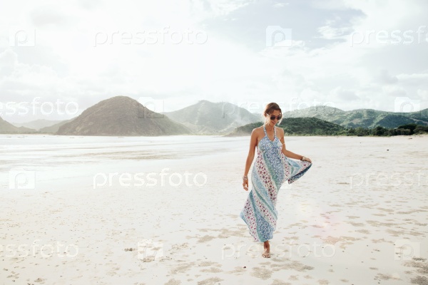 Woman wearing ethnic flying dress walking barefoot at the beach, Lombok, Indonesia, stock photo