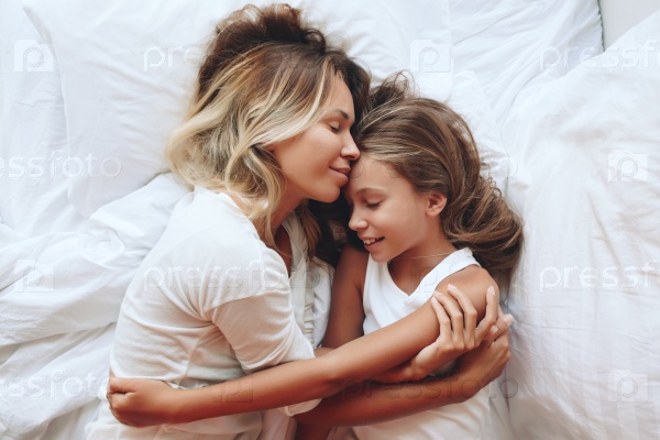 Mom with her tween daughter relaxing in bed, positive feelings, good relations. Top view, stock photo
