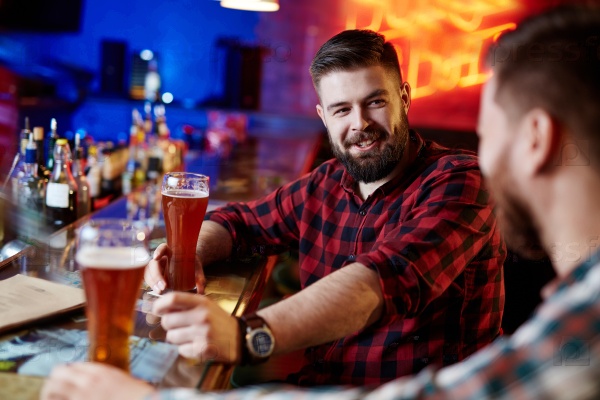 Happy bearded man with beer talking to his friend in pub, stock photo