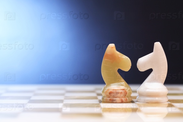 Pair of chess horses made from Onyx on board against blue background, stock photo