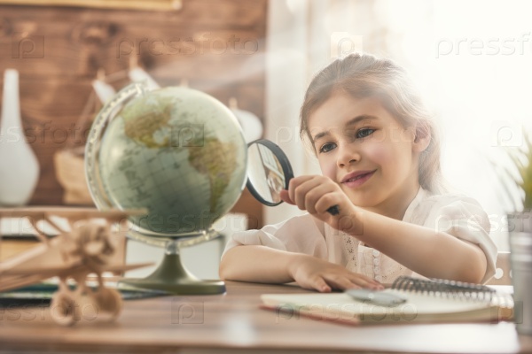 Go on an adventure! Happy cute child preparing for the journey. Pretty girl study the globe and choose a route of travel.