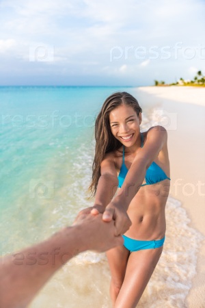 Follow me concept. Asian girlfriend leading man holding hand. Happy multiracial woman in blue bikini with sexy and slim suntan body. Couple in love walking on tropical beach vacations summer travel.