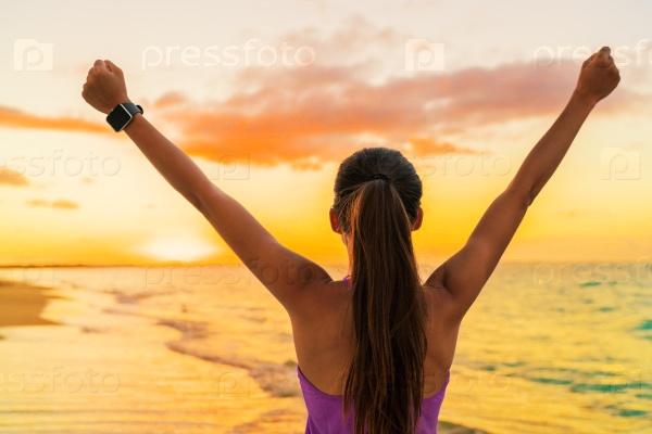 Success freedom smartwatch woman from behind at sunset. Winning goal achievement fitness athlete girl cheering on tropical summer beach wearing wearable tech smart watch activity bracelet.