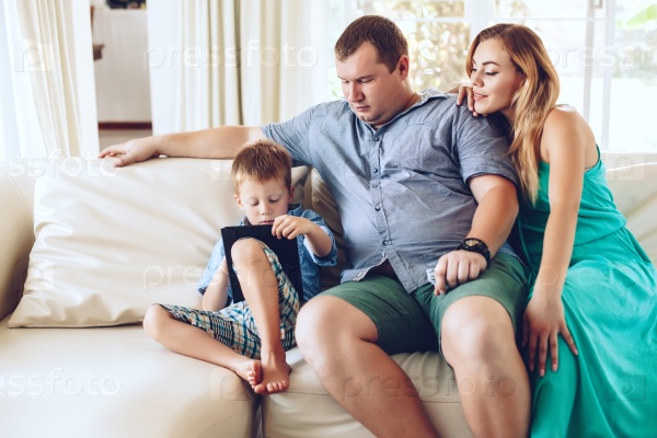 Happy family resting on a sofa and using digital tablet together in living room, stock photo