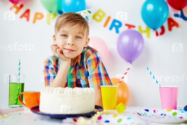 Happy boy looking at camera by birthday cake, stock photo