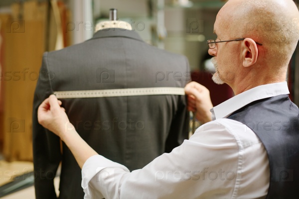 Modern tailor measuring back of jacket on mannequin, stock photo