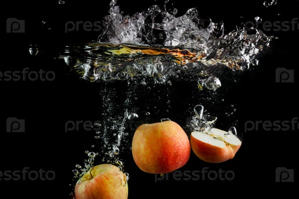 Apples falling into the water with a splash and air bubbles. Fresh apples in water on black background. Healthy food. Wash fruits, stock photo