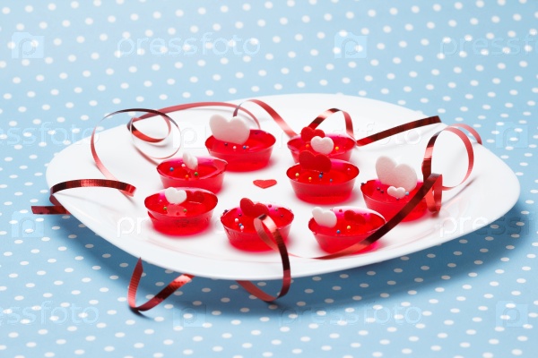 Plate of Valentine\'s day love gelatin deserts with red and white hearts and ribbon on blue with dots (polka dot) background