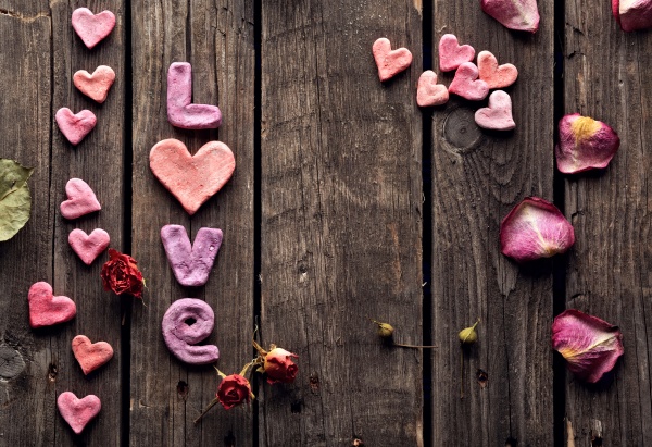 Word Love with rose petals and small heart shaped stuff on old vintage wood plates. Sweet holiday background.