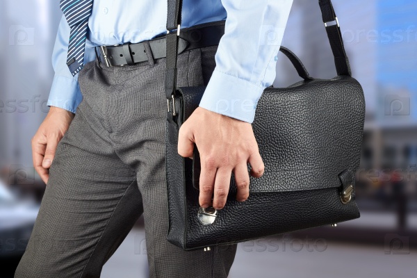 Businessman walking and holding  a  leather briefcase in his hand.  Modern city behind