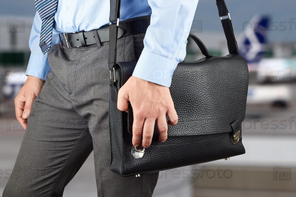 Businessman walking and holding  a  leather briefcase in his hand. airport  behind