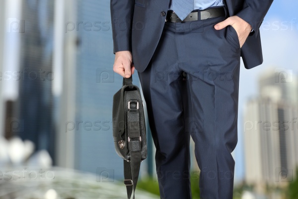 Businessman walking and holding  a  leather briefcase in his hand. Modern city behind