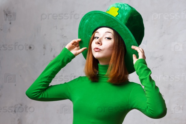Red hair girl in Saint Patrick\'s Day leprechaun party hat having fun isolated on grey grunge background