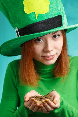 Red hair girl in Saint Patrick\'s Day party hat having fun with gold coins isolated on green grunge background