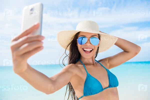 Selfie smartphone girl taking mobile phone photo on beach vacation during summer travel holidays. Sexy young bikini woman wearing fashion mirrored aviator sunglasses posing for camera having fun.