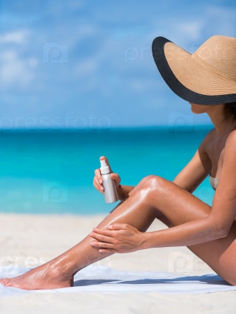 Sunscreen suntan lotion spray skincare product closeup of woman putting tanning oil on her legs. Hand holding sunblock or mosquito repellent bottle spraying on body sunbathing at beach summer vacation