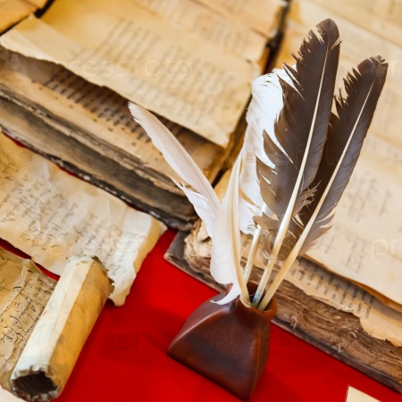 feathers and inkpot with Old books on the red tablecloth