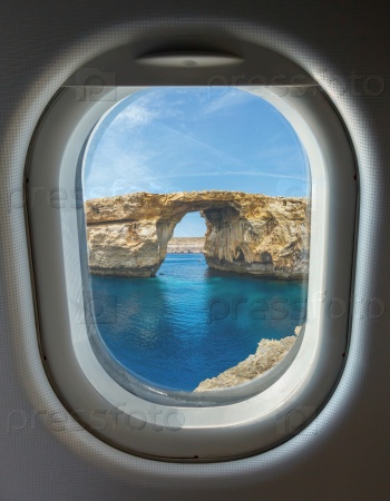 porthole and landmark, Azure Window, famous stone arch of Gozo island through the window of the plane against the blue sky on a clear day, Malta