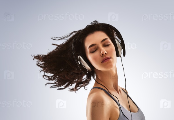 beautiful young woman listening music in headphones on a gray background. the girl is resting and enjoys the music.