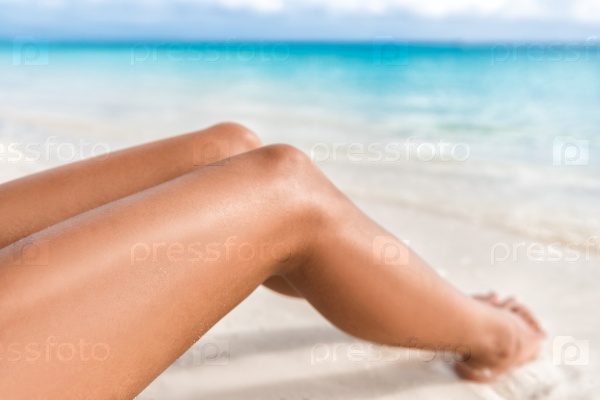 Sexy suntan bikini woman legs relaxing lying down on white sand beach summer vacation. Beauty skincare sun aging protection body care of tanned skin. Epilation laser or shaving concept.